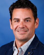 Man with dark grey hair, a light shirt and a dark jacket.