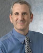 Man with short gray hair wearing a blue button-down shirt and a gray tie